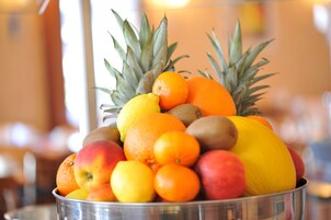 Un tazón metálico lleno de frutas variadas, incluyendo naranjas, manzanas y kiwis.
