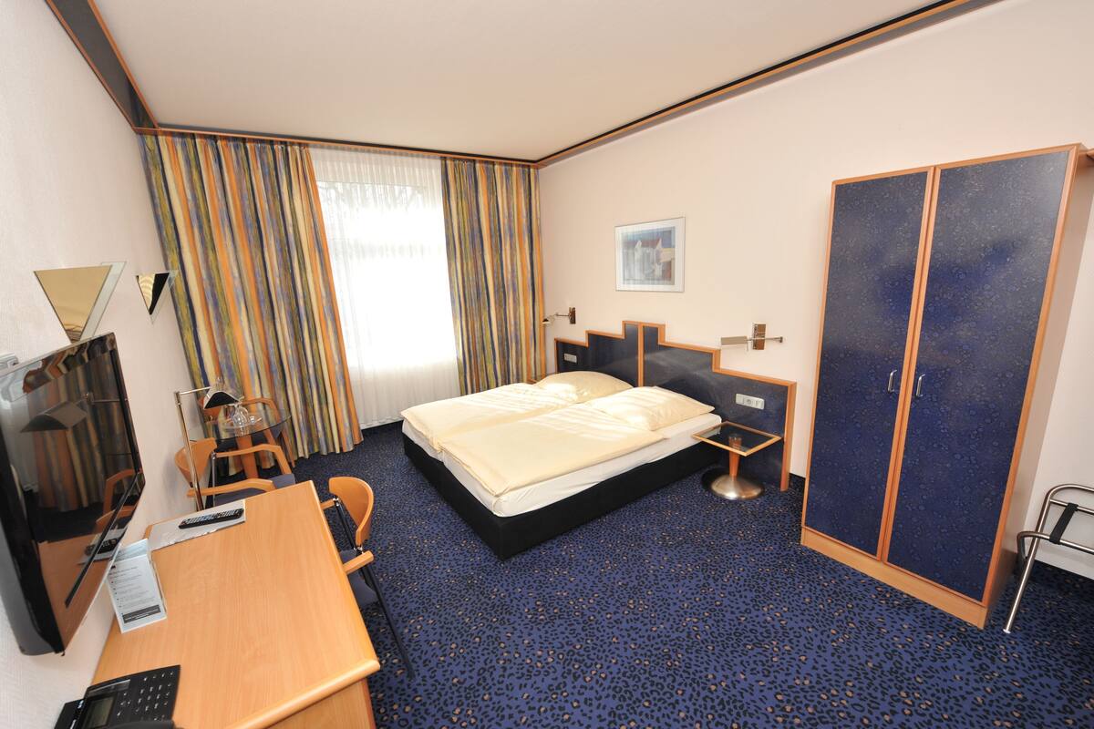 Ein Hotelzimmer mit Bett, Schreibtisch, Stuhl und Kleiderschrank.