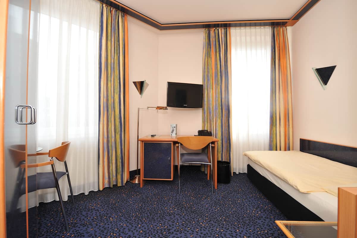 Ein Hotelzimmer mit Bett, Schreibtisch, Stuhl, Fernseher und Vorhängen.