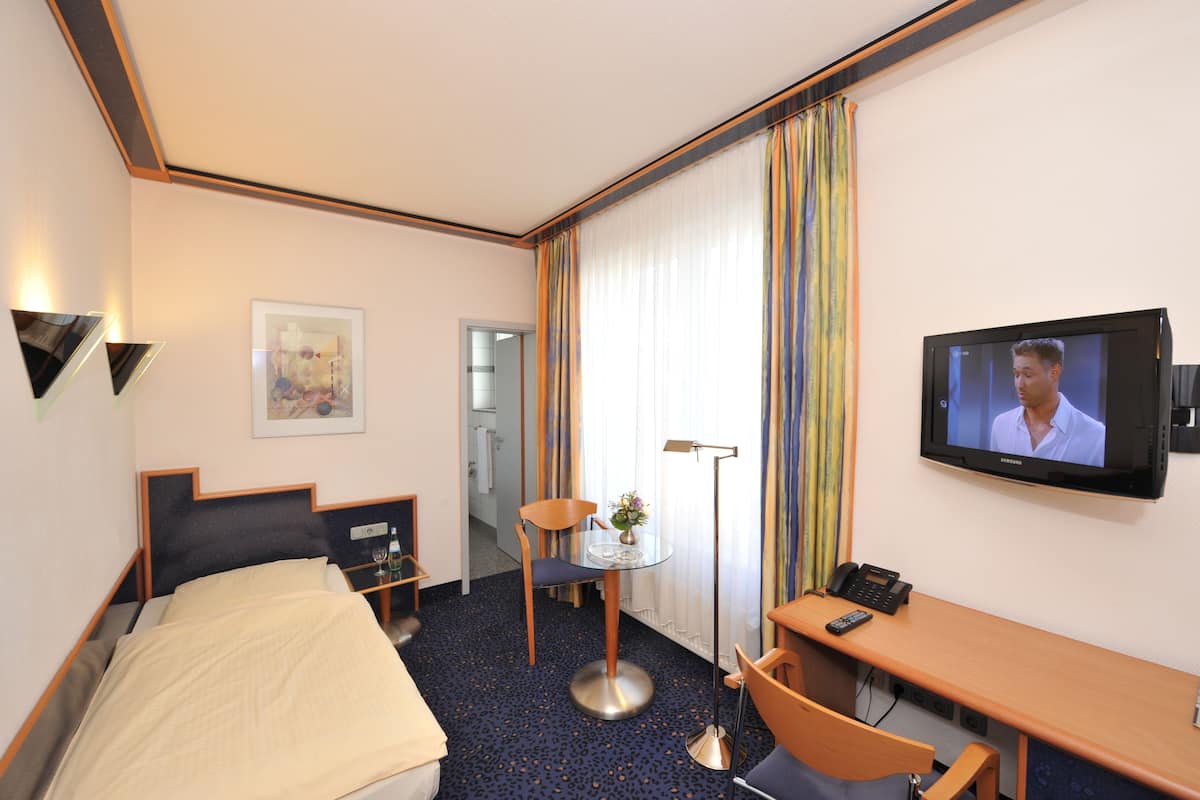 Ein Hotelzimmer mit Bett, Schreibtisch, Stuhl, Fernseher und einem kleinen Tisch mit einer Vase.