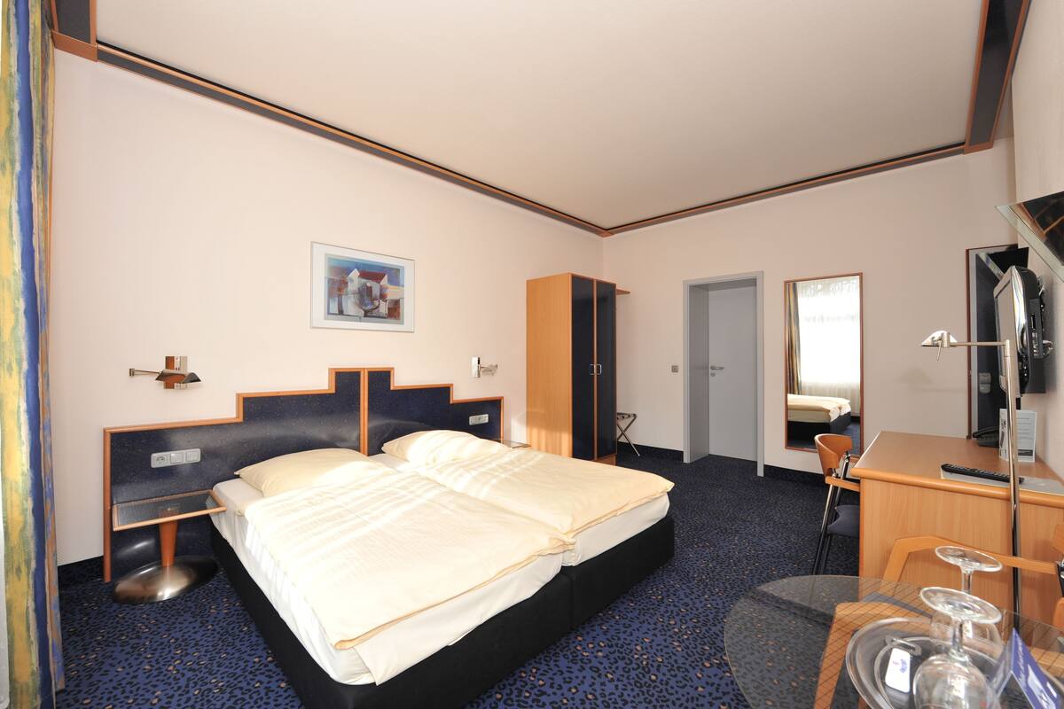 Ein Hotelzimmer mit einem Doppelbett, einem Schreibtisch mit Stuhl, einem Fernseher und einem Spiegel.