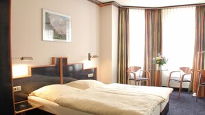 A hotel room with a large bed, a desk, two chairs, a small table, and a window with curtains. - Insel Hotel (Cologne)