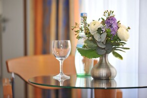Una mesa de vidrio con un jarrón de flores y una copa de vino.