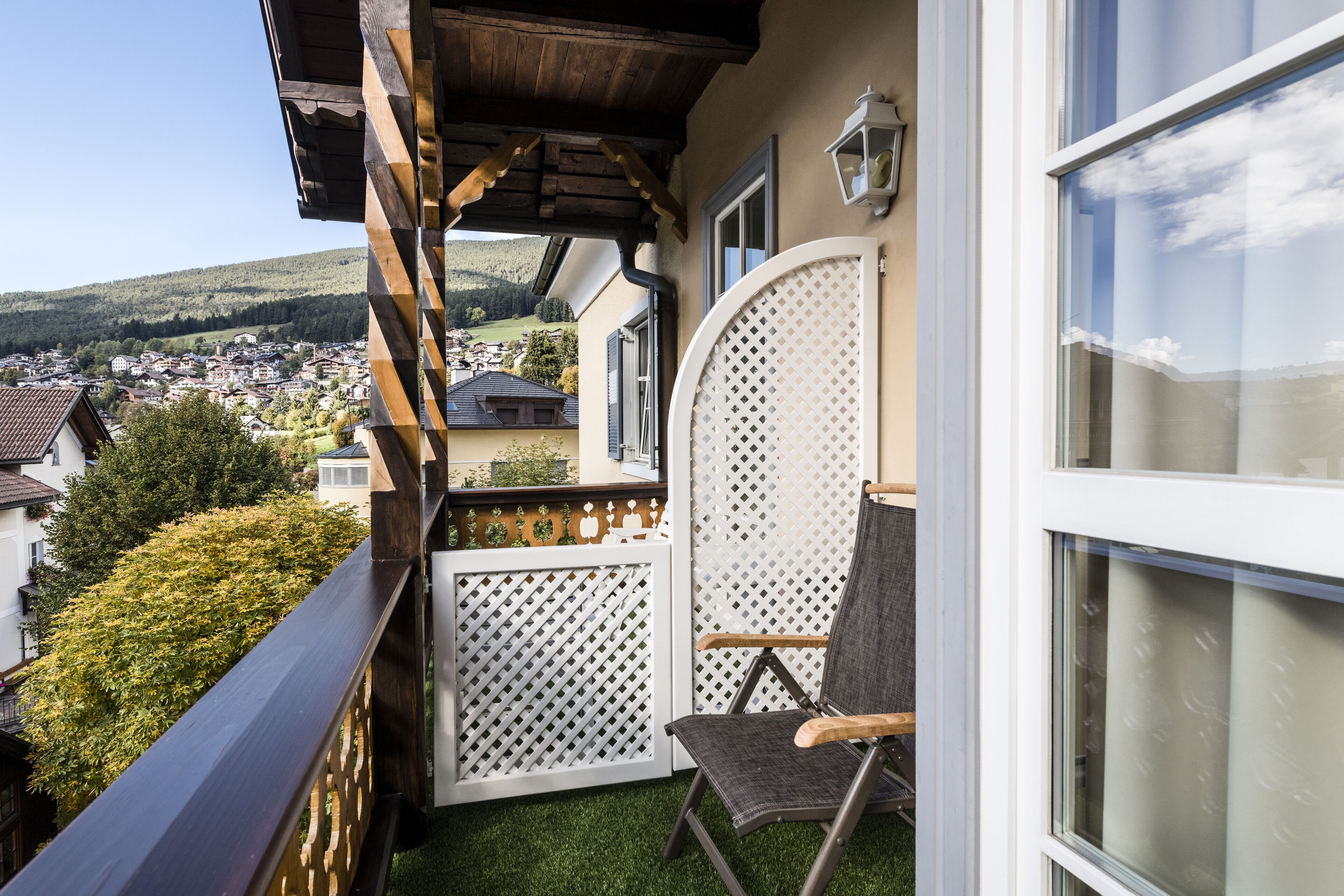 A balcony with a wooden railing, a white lattice partition, and a chair.