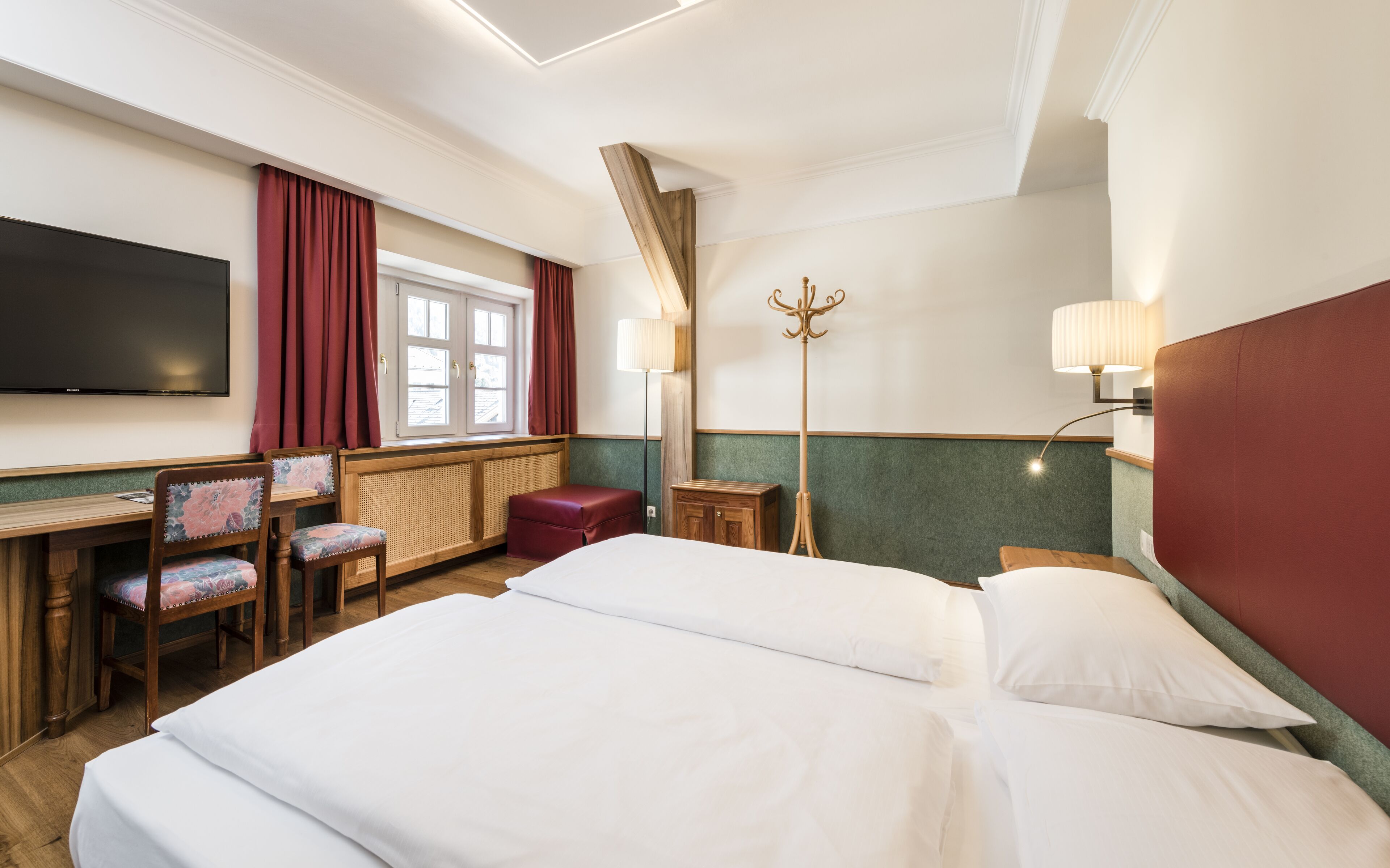 Habitación de hotel con cama, escritorio, silla, televisor y ventana con cortinas.
