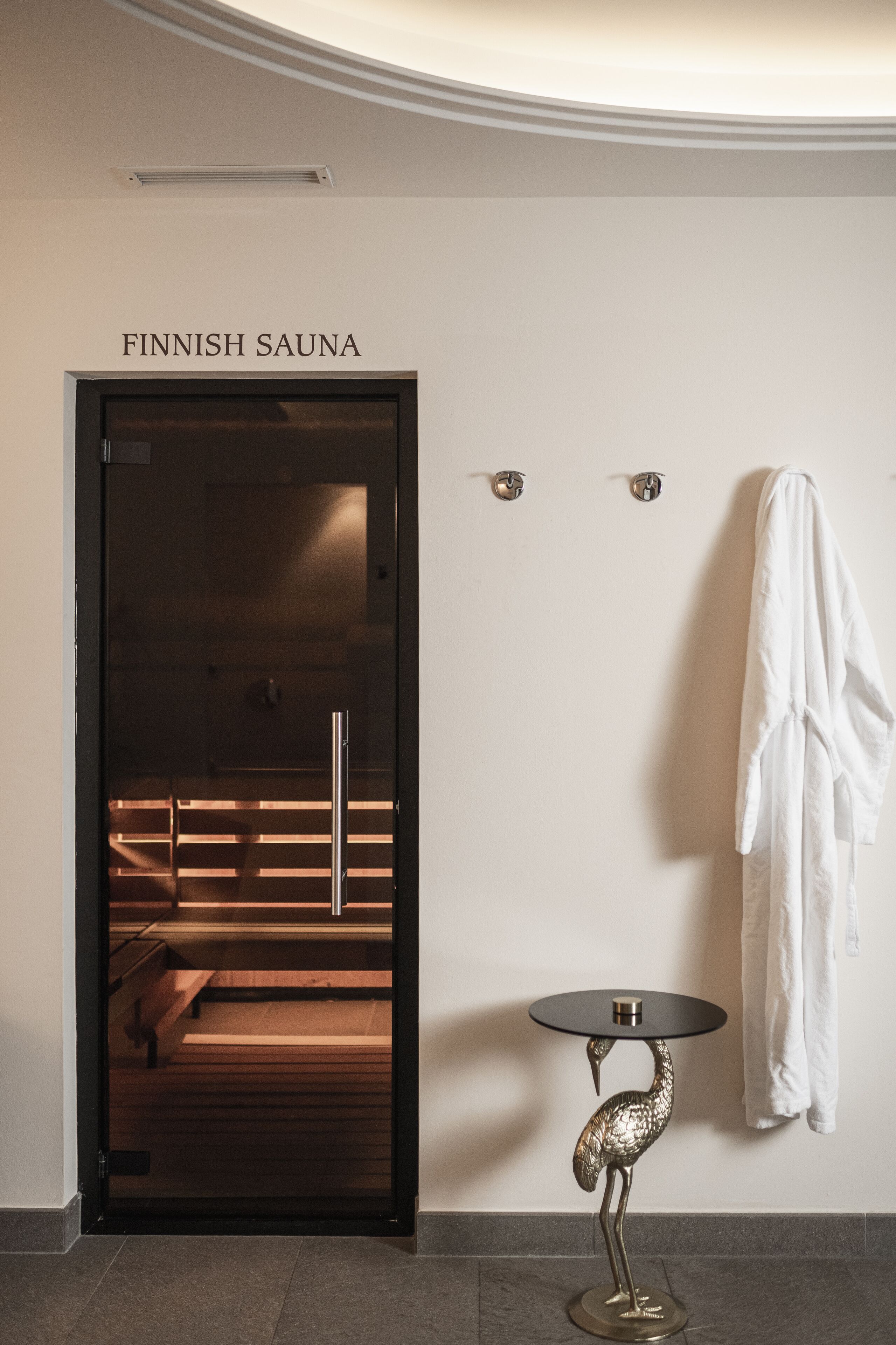 A Finnish sauna room with a glass door, a wooden bench inside, and a white towel hanging on the wall.