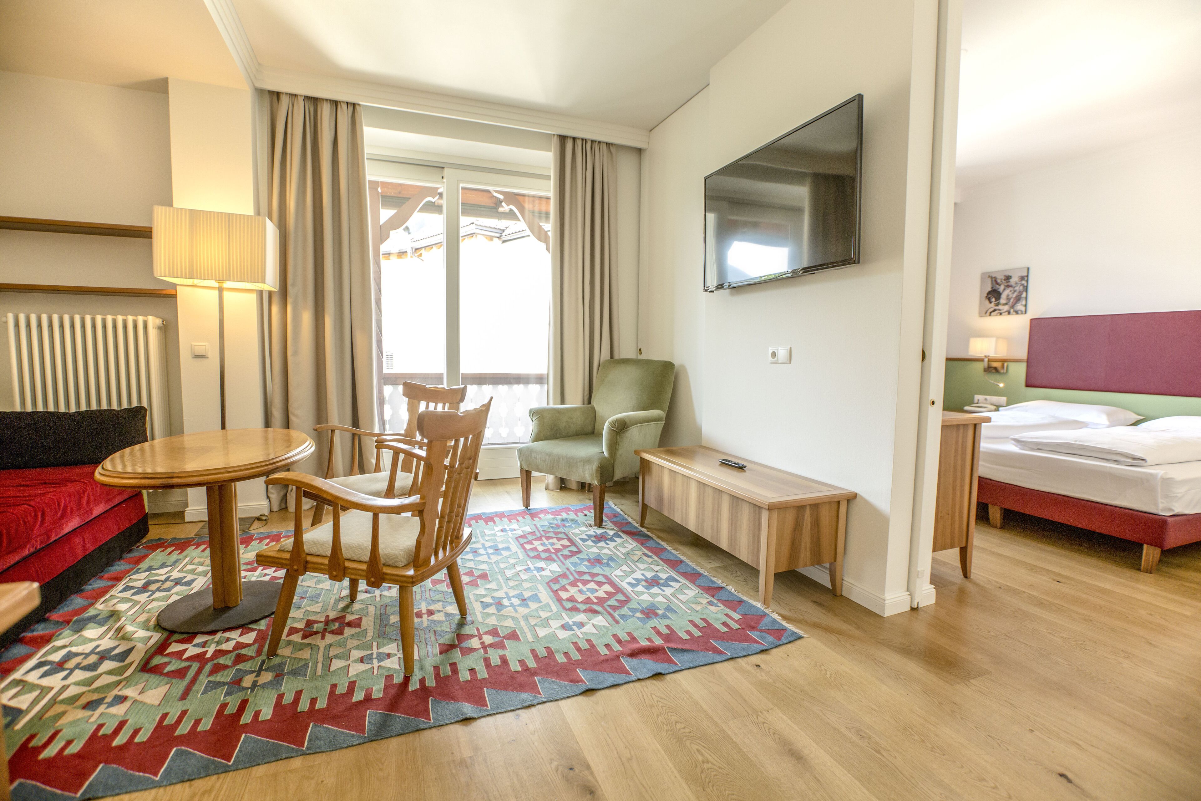 A hotel room with a bed, a desk, a chair, a sofa, a TV, and a window with curtains.