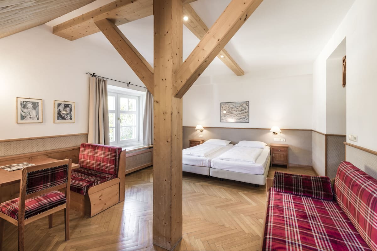 A room with a wooden ceiling, two beds, a table, and chairs.