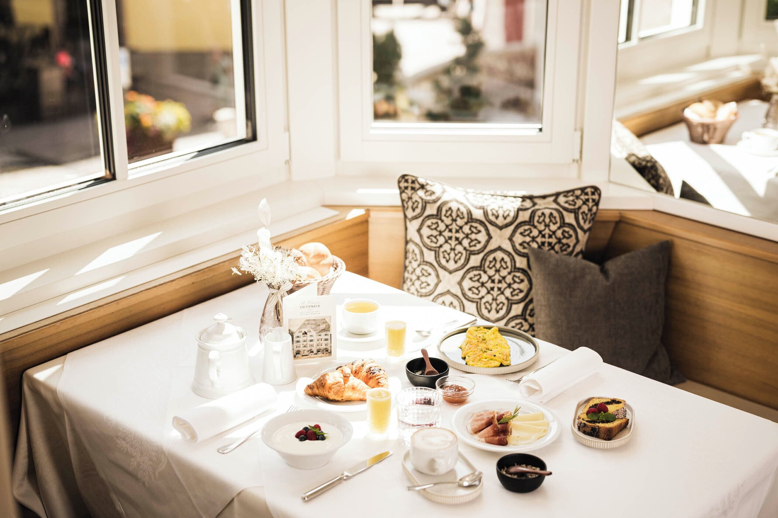 Ein Frühstückstisch für zwei Personen mit Croissants, einem Becher Joghurt mit Beeren und einem Teller Rührei.