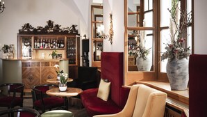 Een bar met een houten toonbank, rode fauteuils en een groot raam met uitzicht op bomen.