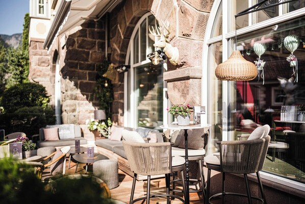 An outdoor seating area with wicker furniture, a stone building, and a large window.