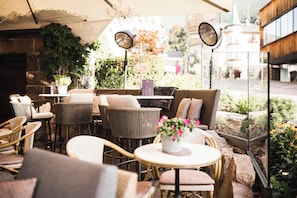 An outdoor seating area with wicker chairs, round tables, and a variety of plants. - Classic Hotel am Stetteneck (Ortisei)