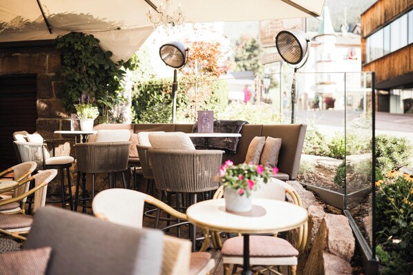 An outdoor seating area with wicker chairs, round tables, and a variety of plants.