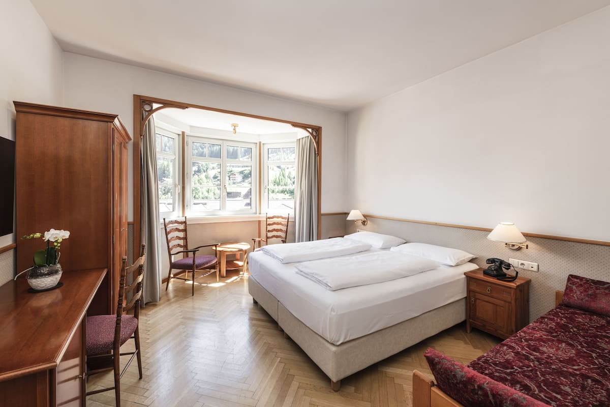 A hotel room with a bed, a desk, a chair, a small table, and a window with curtains.