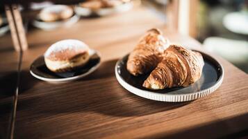 A wooden table with two plates of pastries, one with a round pastry and the other with a croissant.