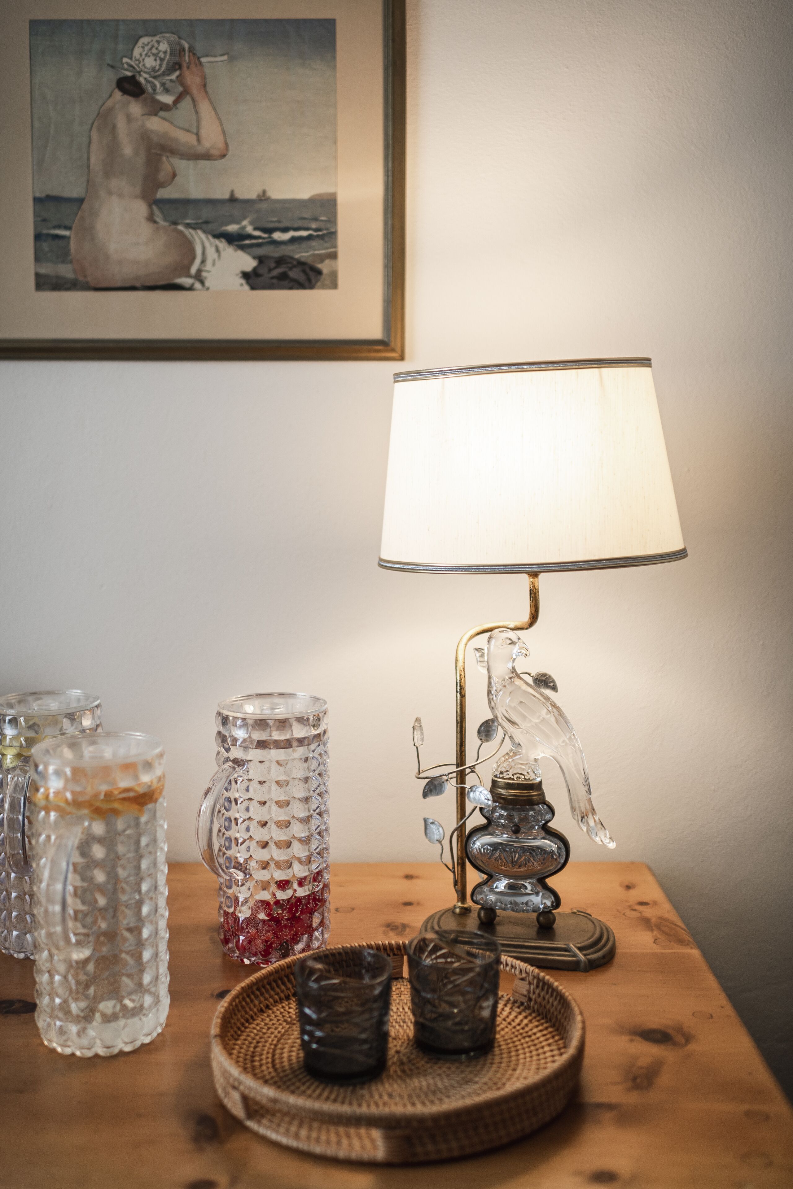 Une table avec une lampe, un tableau encadré et des objets en verre décoratifs.