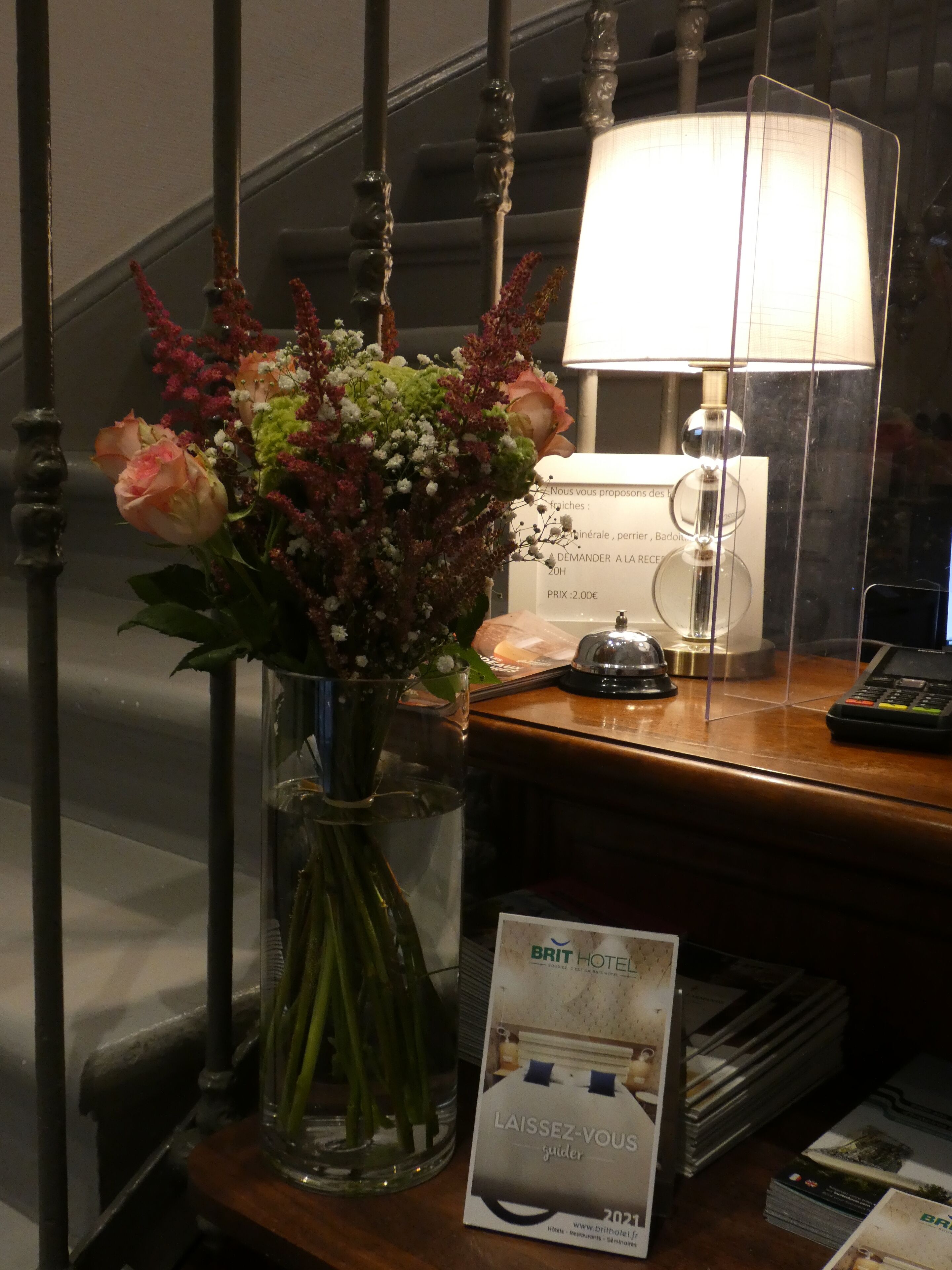 Un comptoir d’accueil orné d’un vase de fleurs, d’une lampe et d’une brochure.