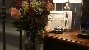 Un comptoir d’accueil orné d’un vase de fleurs, d’une lampe et d’une brochure.