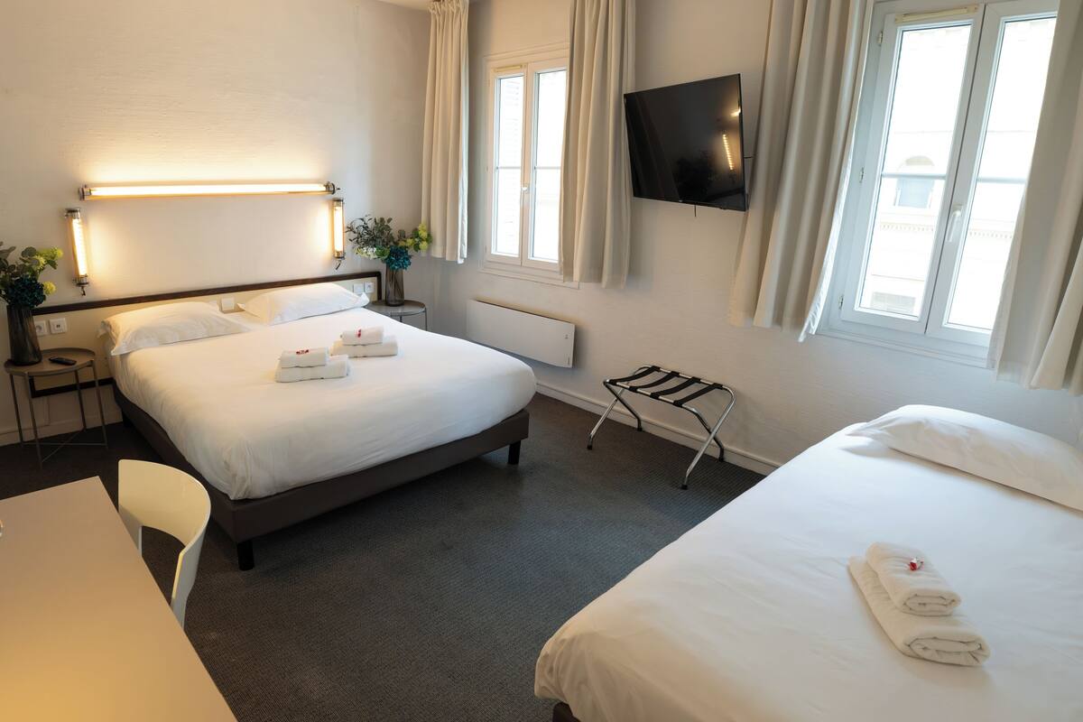 A hotel room with a bed, bedside tables, a desk, a chair, a TV, and a window with curtains.