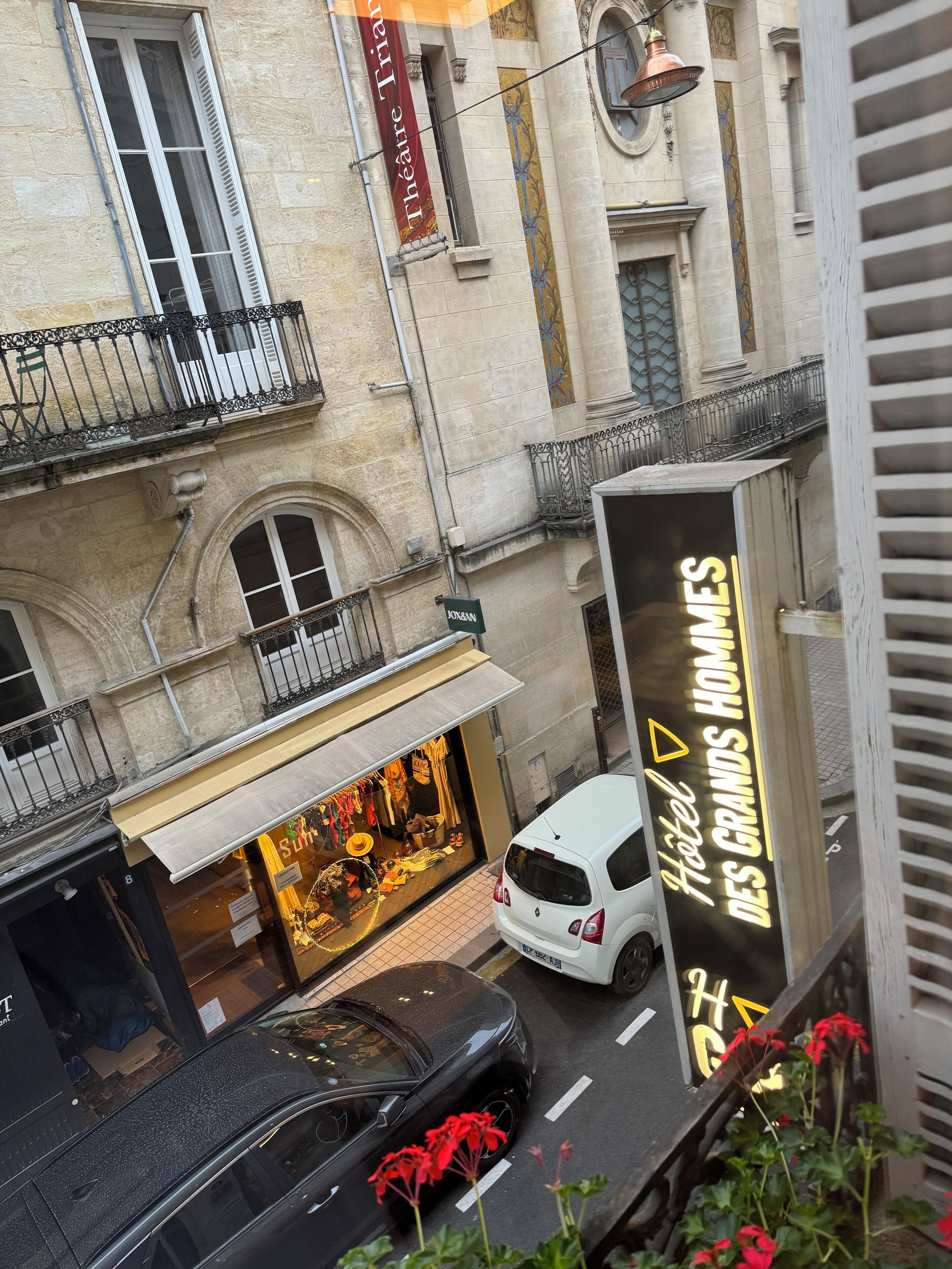 Vista de la calle con un hotel boutique llamado 'Hotel des Grands Hommes' y una tienda llamada 'Joxan' mostrando una exhibición de joyería.