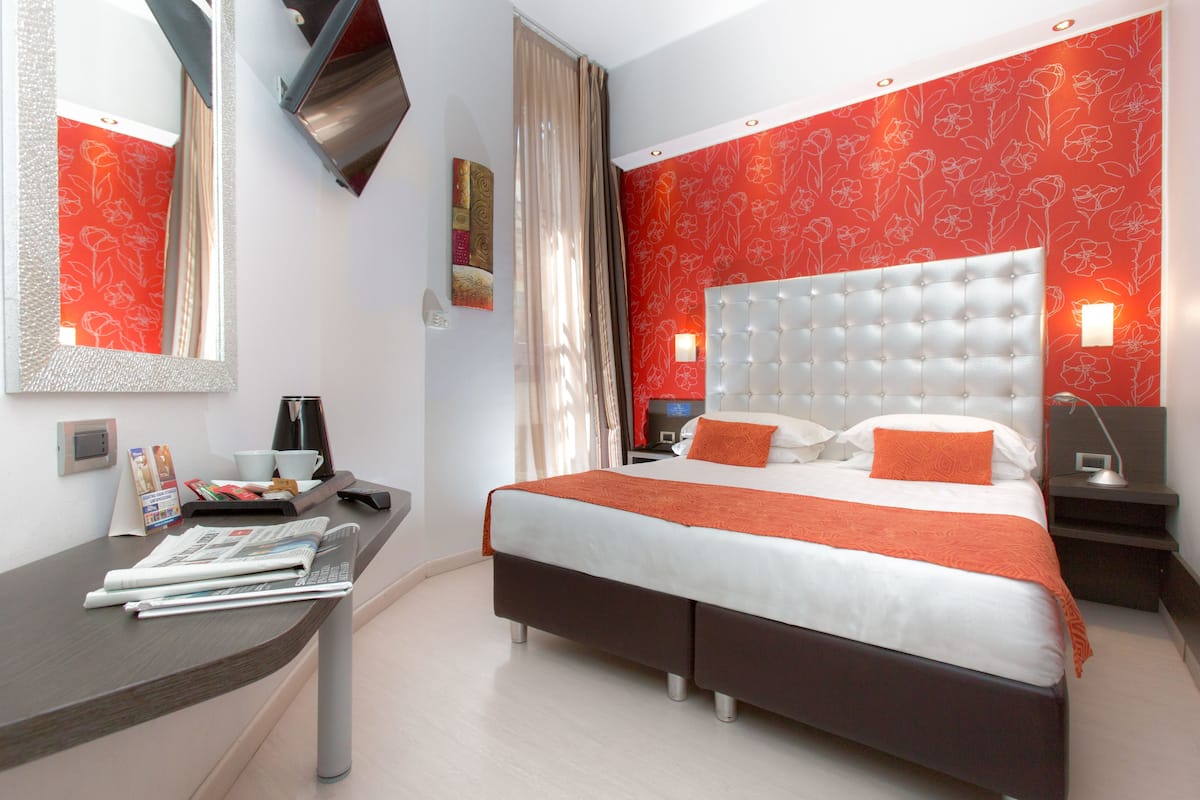 A modern hotel room with a large bed, a desk with a chair, and a mirror.