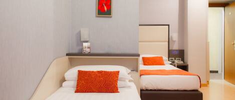 A hotel room with two beds, each with white bedding and orange accents. There is a small table with a telephone and a wall-mounted light.