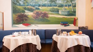 A room with a large landscape painting on the wall, two tables with tea sets, and a blue sofa. - Hotel Piacenza (Milan)