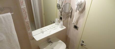 A bathroom with a sink, a mirror, a hairdryer, and a towel hanging on a rack.