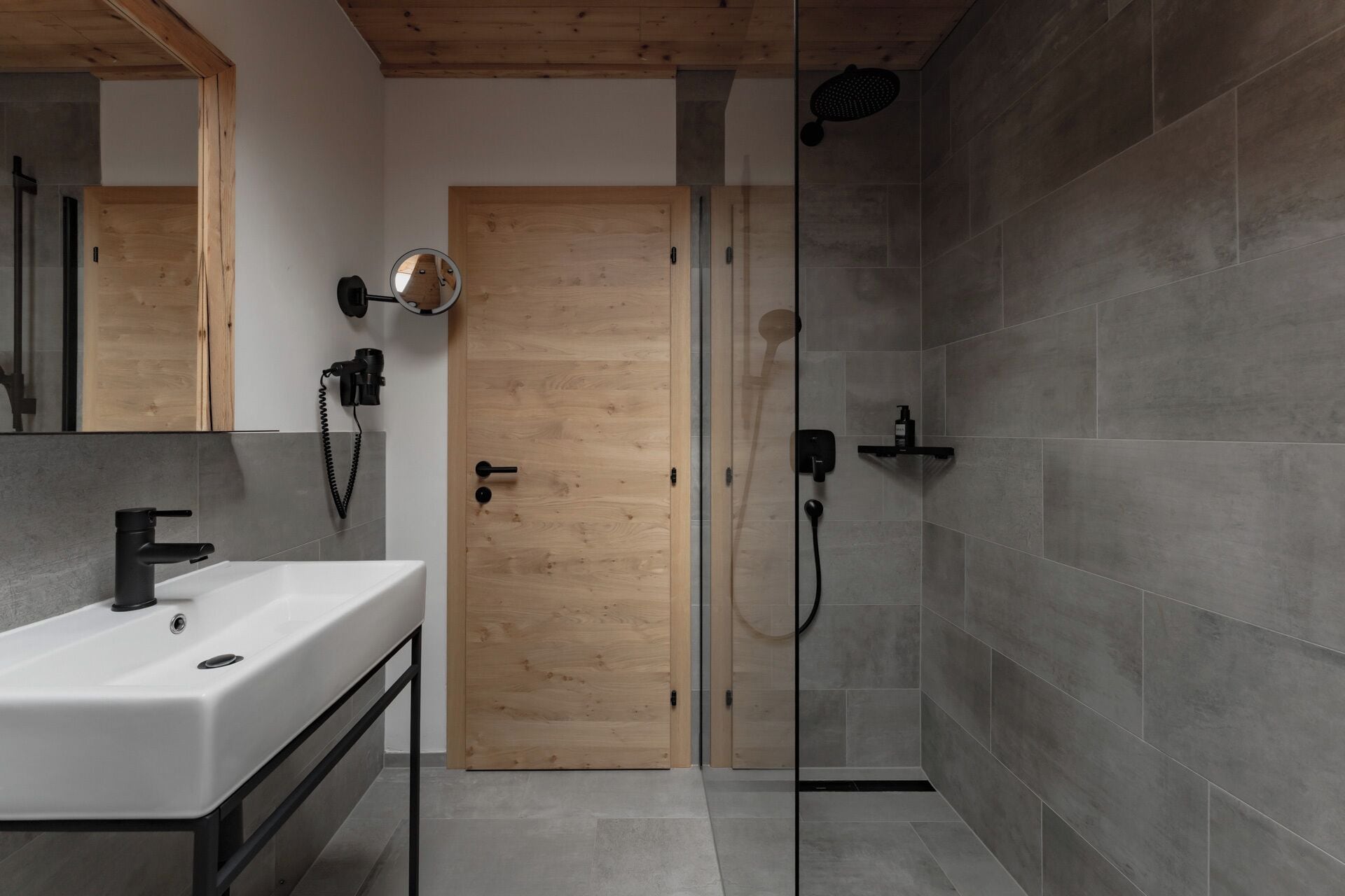 Une salle de bain moderne avec une porte en bois, une douche en verre et un lavabo blanc doté d’un robinet noir.