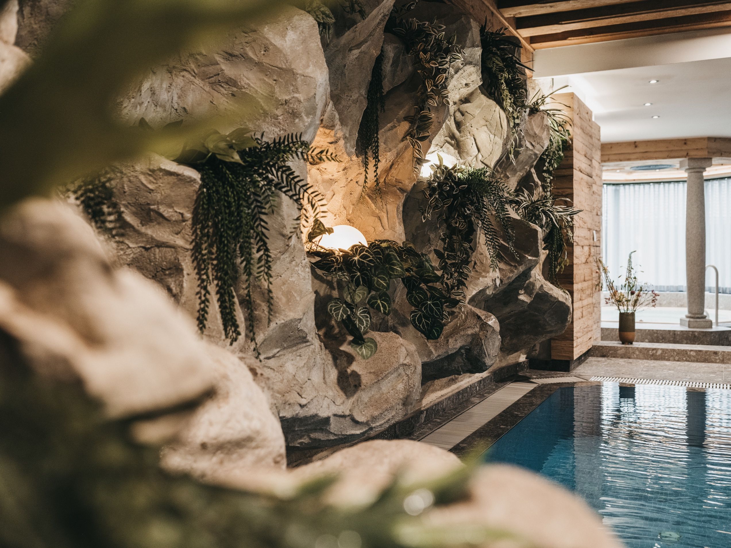 Un espace piscine agrémenté d’un mur rocheux orné de différentes plantes.