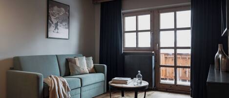 Un salon avec un canapé, une table basse, un tableau encadré et une grande fenêtre avec des rideaux.
