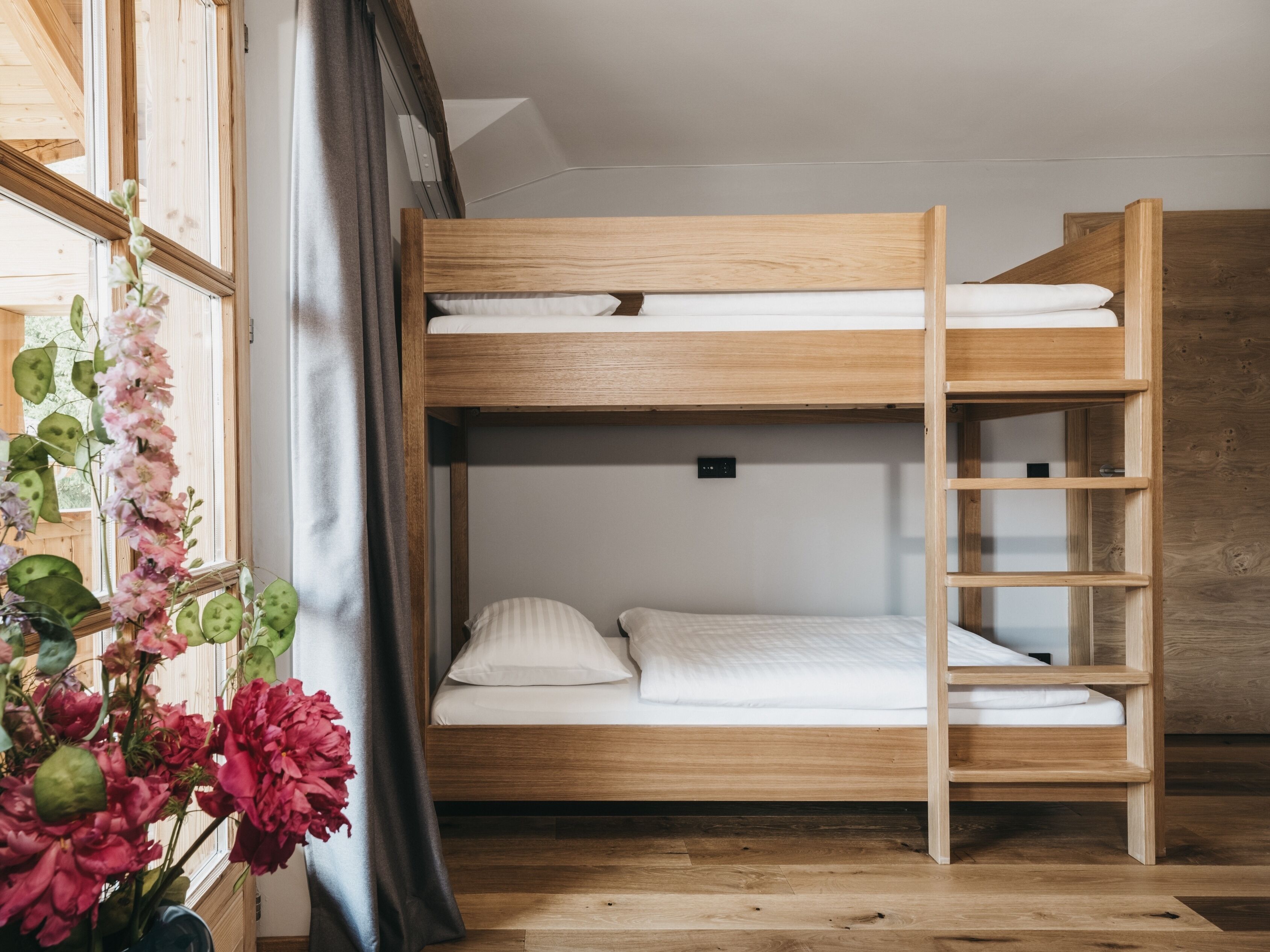 Una cama litera con estructura de madera, una escalera y un estante pequeño.