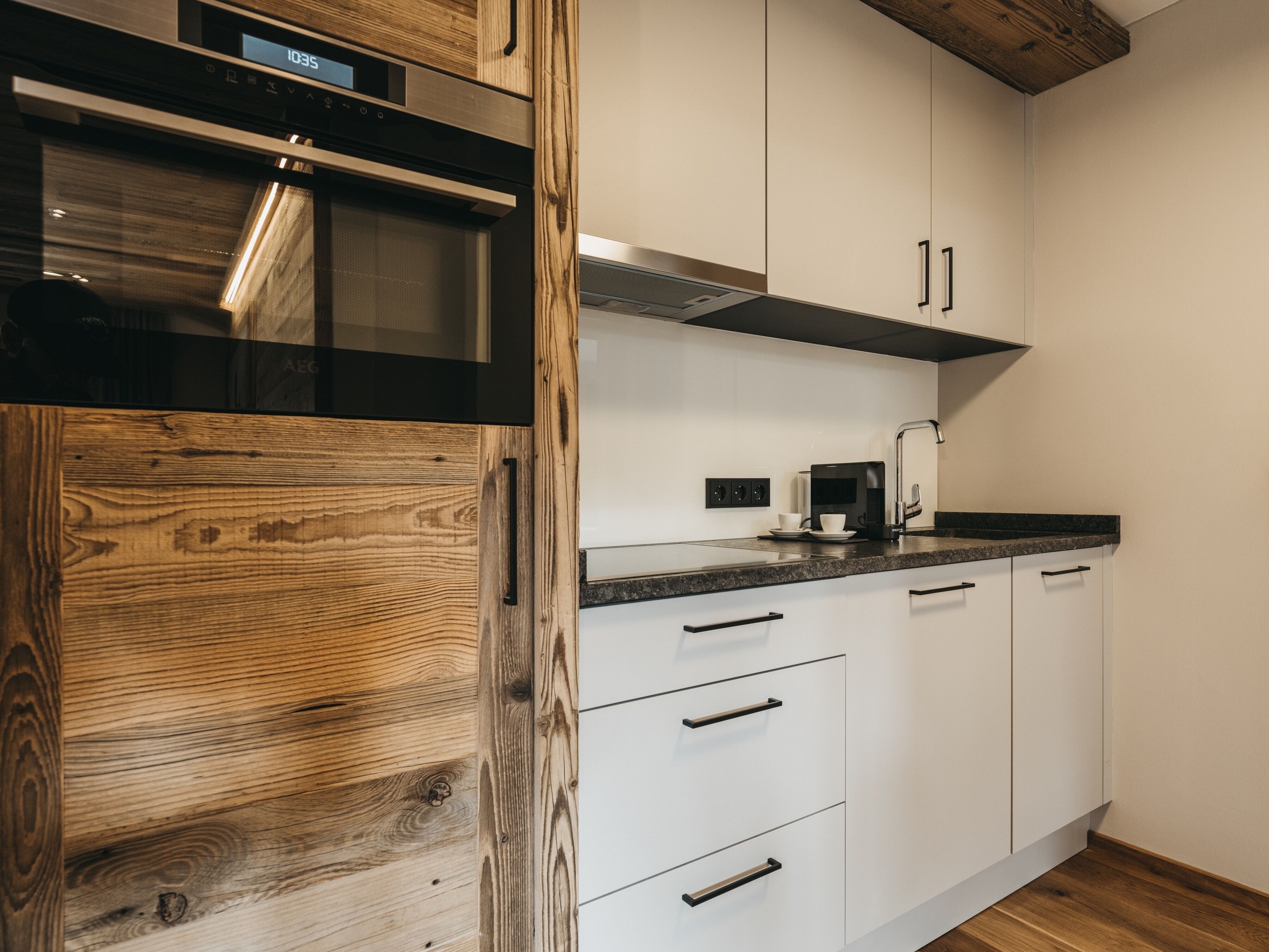 Une cuisine moderne avec des armoires blanches, un micro-ondes noir et un mur d’accent en bois.