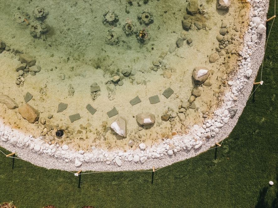 An aerial view of a circular water feature with a pebble border and a grassy edge.