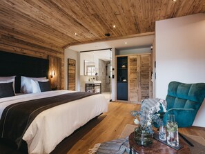 A modern bedroom with a wooden ceiling, a large bed with white and dark bedding, a bedside table with a vase, and a teal armchair. - VAYA Achensee (Achenkirch)