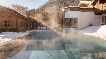 Un área de spa con un jacuzzi rodeado de construcciones de madera y suelo cubierto de nieve.