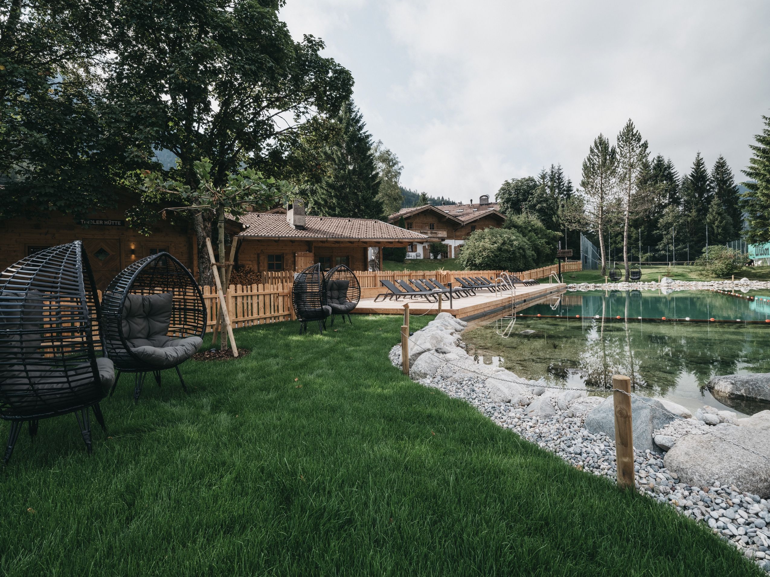 A wooden house with a swimming pool, surrounded by grass and trees.