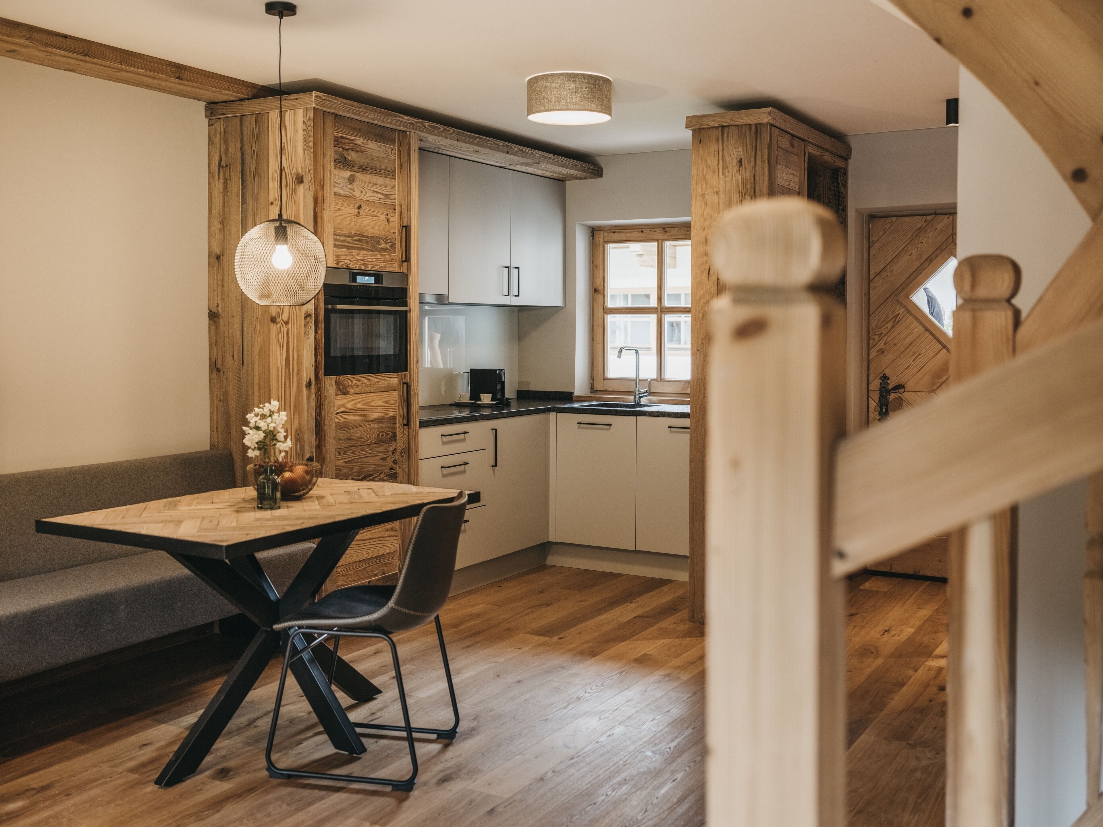 Una cocina moderna con detalles de madera, una mesa de comedor con sillas y una escalera que sube a otro nivel.
