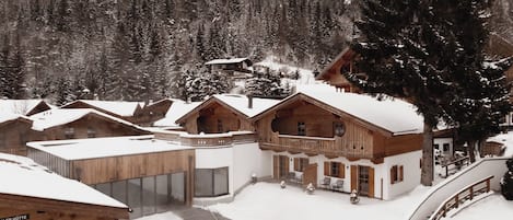 A snow-covered mountain resort with wooden cabins, a pool, and a ski lift.