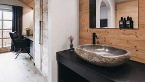 A modern bathroom with a stone sink, wooden accents, and a large mirror reflecting the room. - VAYA Achensee (Achenkirch)