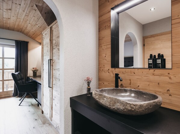 Un baño moderno con lavamanos de piedra, detalles de madera y un espejo grande que refleja la habitación.
