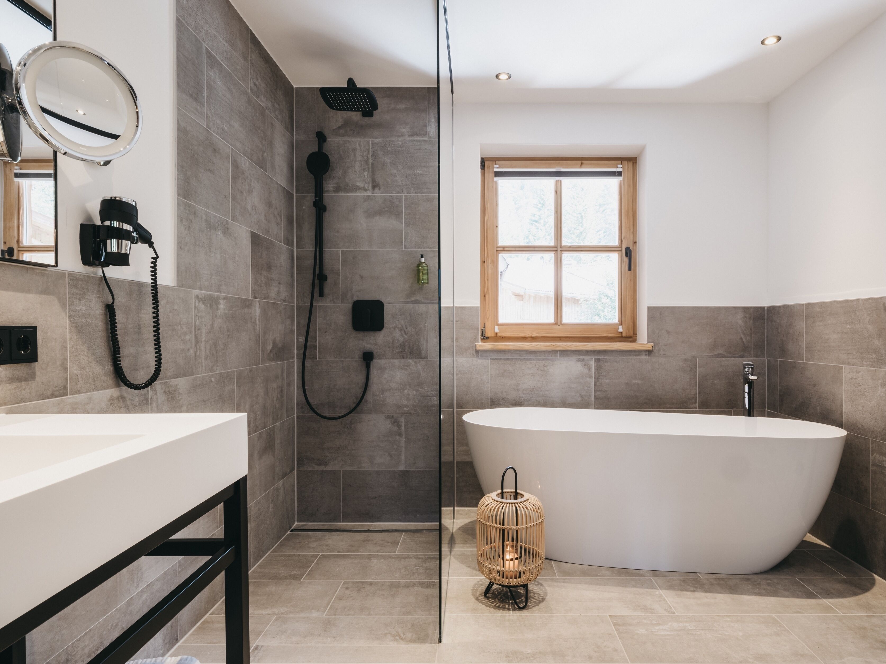 A modern bathroom with a freestanding bathtub, a glass-enclosed shower, and a window providing natural light.