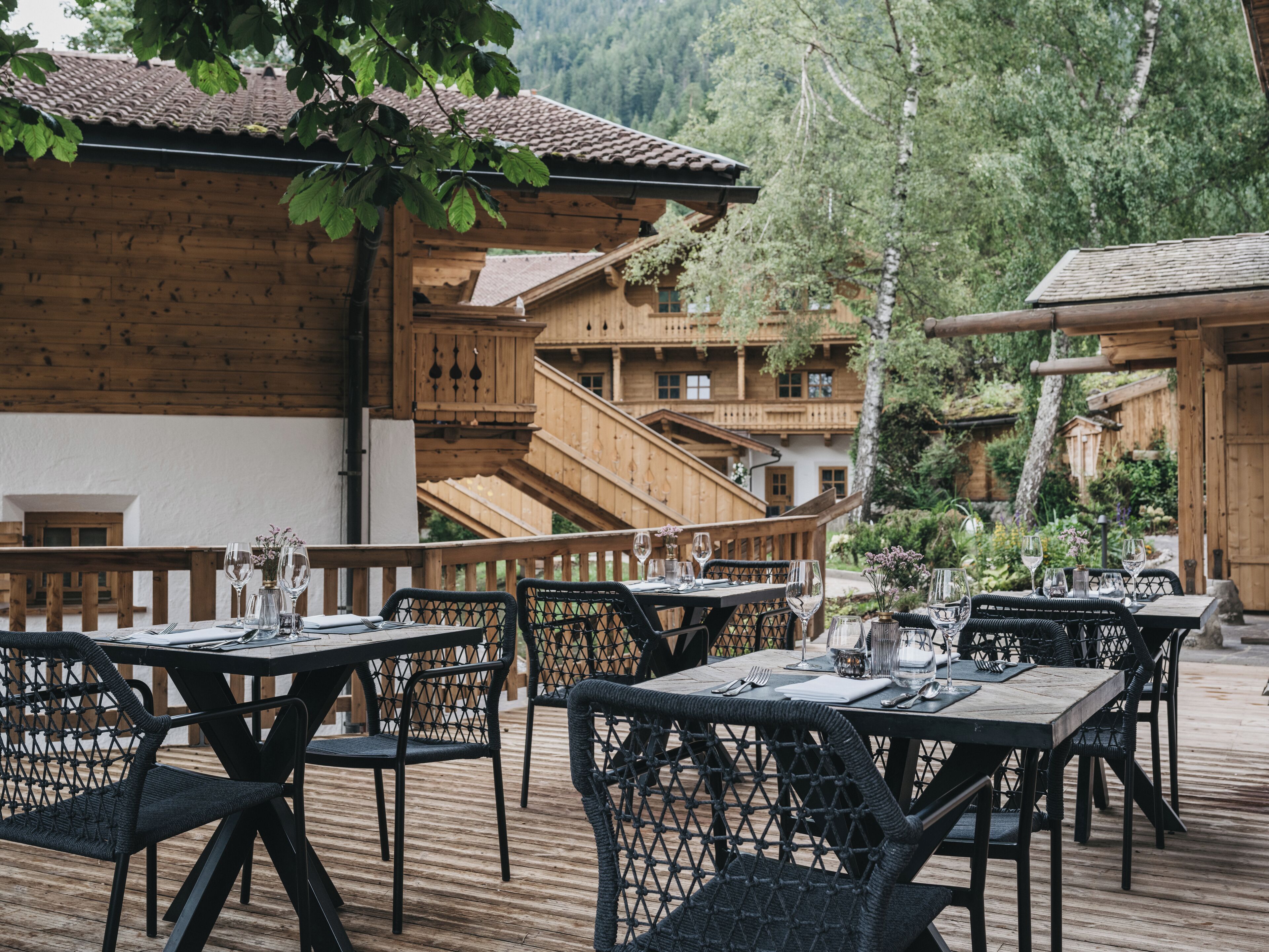 Ein Außenbereich zum Essen mit Holztischen und -stühlen, umgeben von einem Holzzaun und mit Blick auf eine Berglandschaft.
