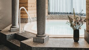 A spa area with a stone column, a wooden ceiling, and a view of a pool through a window. - VAYA Achensee (Achenkirch)