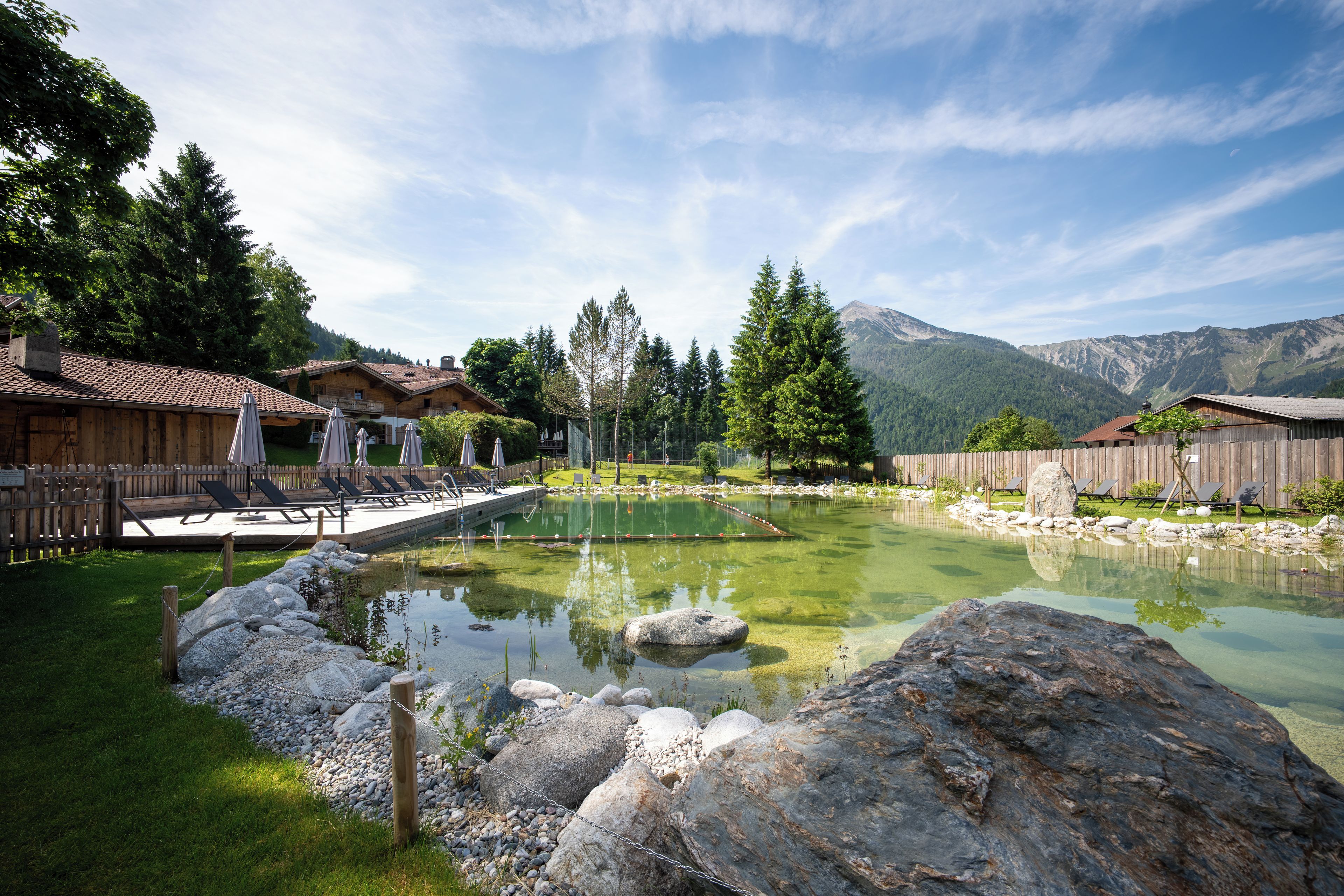 A mountain resort with a clear pond, wooden chalets, and a view of the mountains.