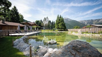 A mountain resort with a clear pond, wooden chalets, and a view of the mountains.