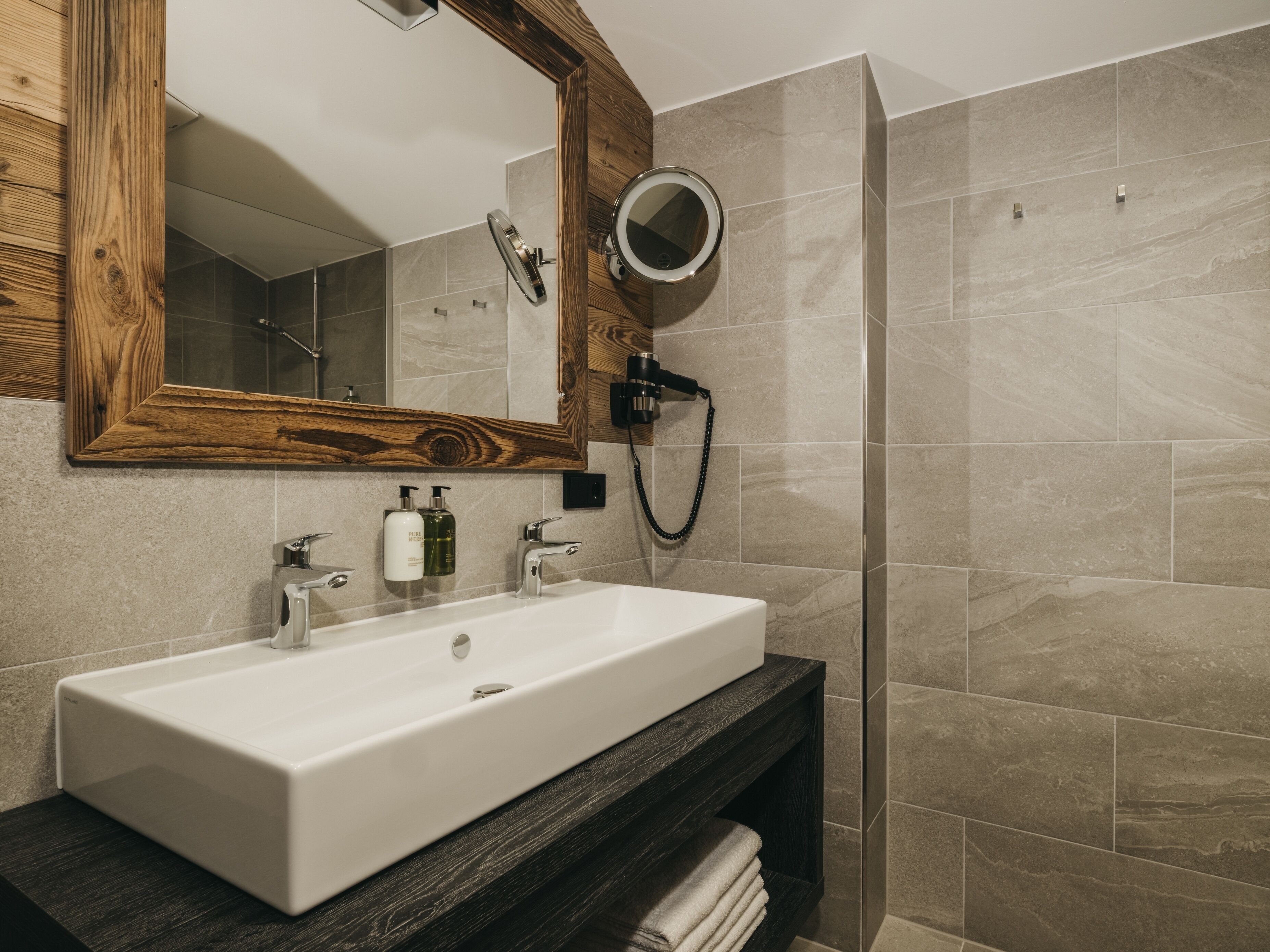 Een moderne badkamer met een grote spiegel, een wit wastafelmeubel, een handdouche en een houten opbergkast.