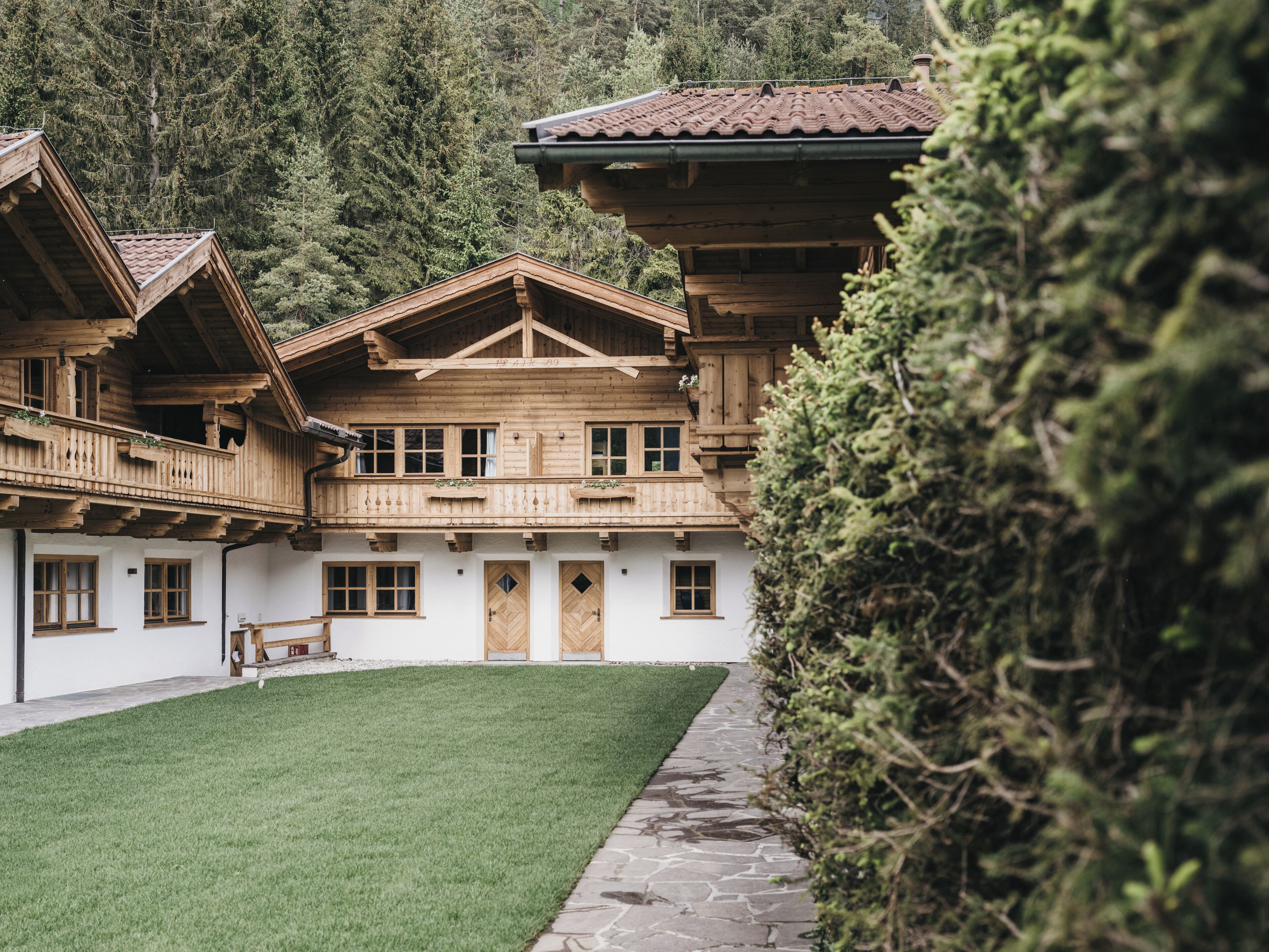 A traditional wooden chalet with a balcony, a stone pathway, and a well-maintained lawn.