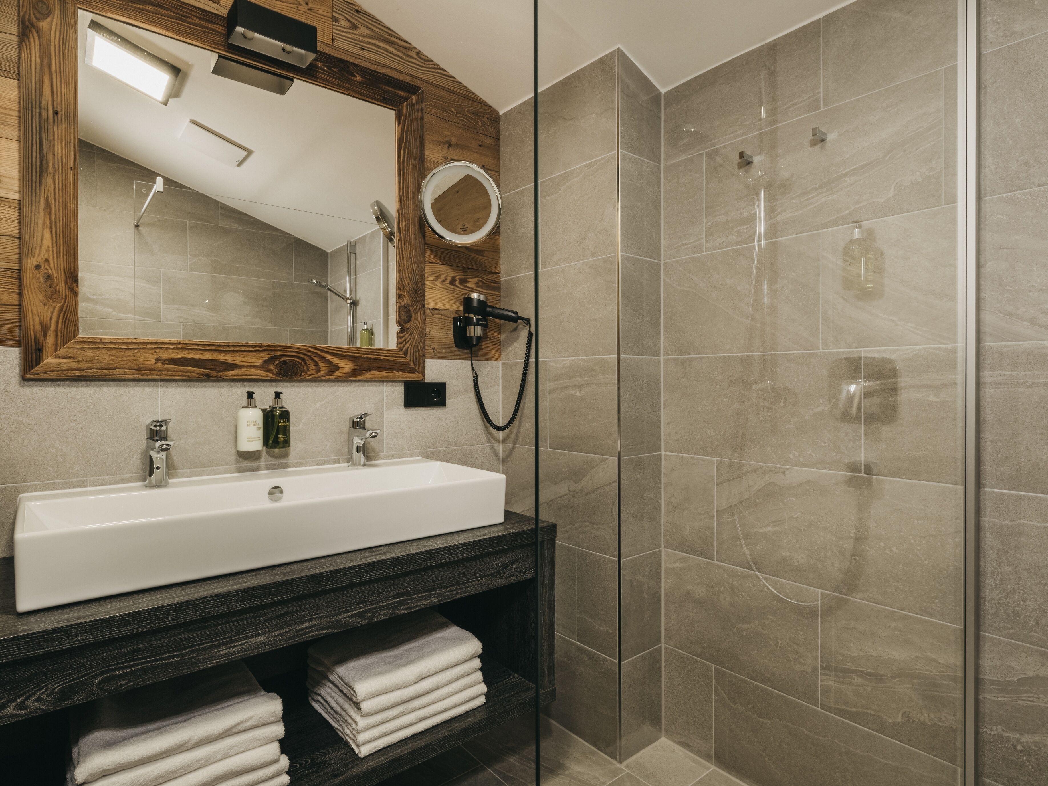 A modern bathroom with a large mirror, a white sink, and a glass-enclosed shower.