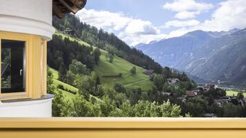 Un balcón con mesa y sillas, con vista a un paisaje montañoso con casas y vegetación.